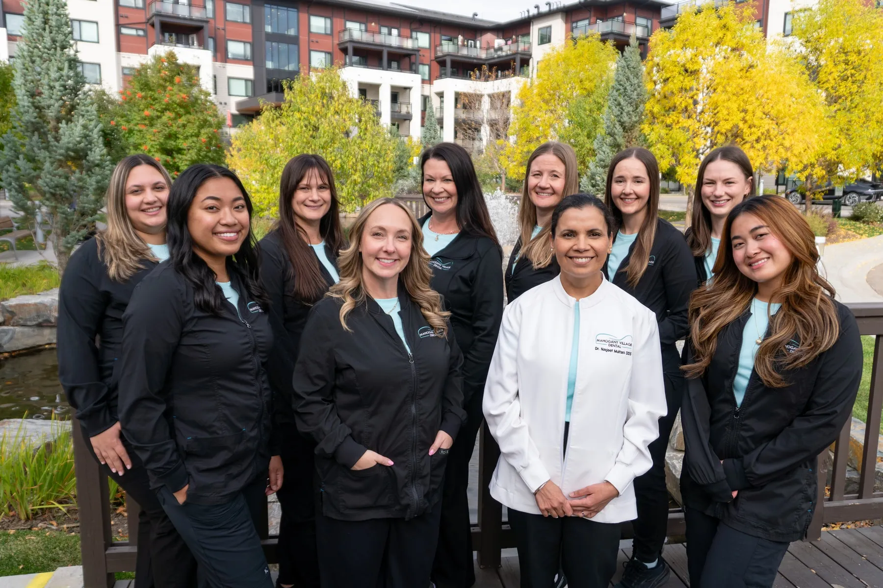 The Mahogany Village Dental team gathered on a wooden bridge in front of the Mahogany village pond