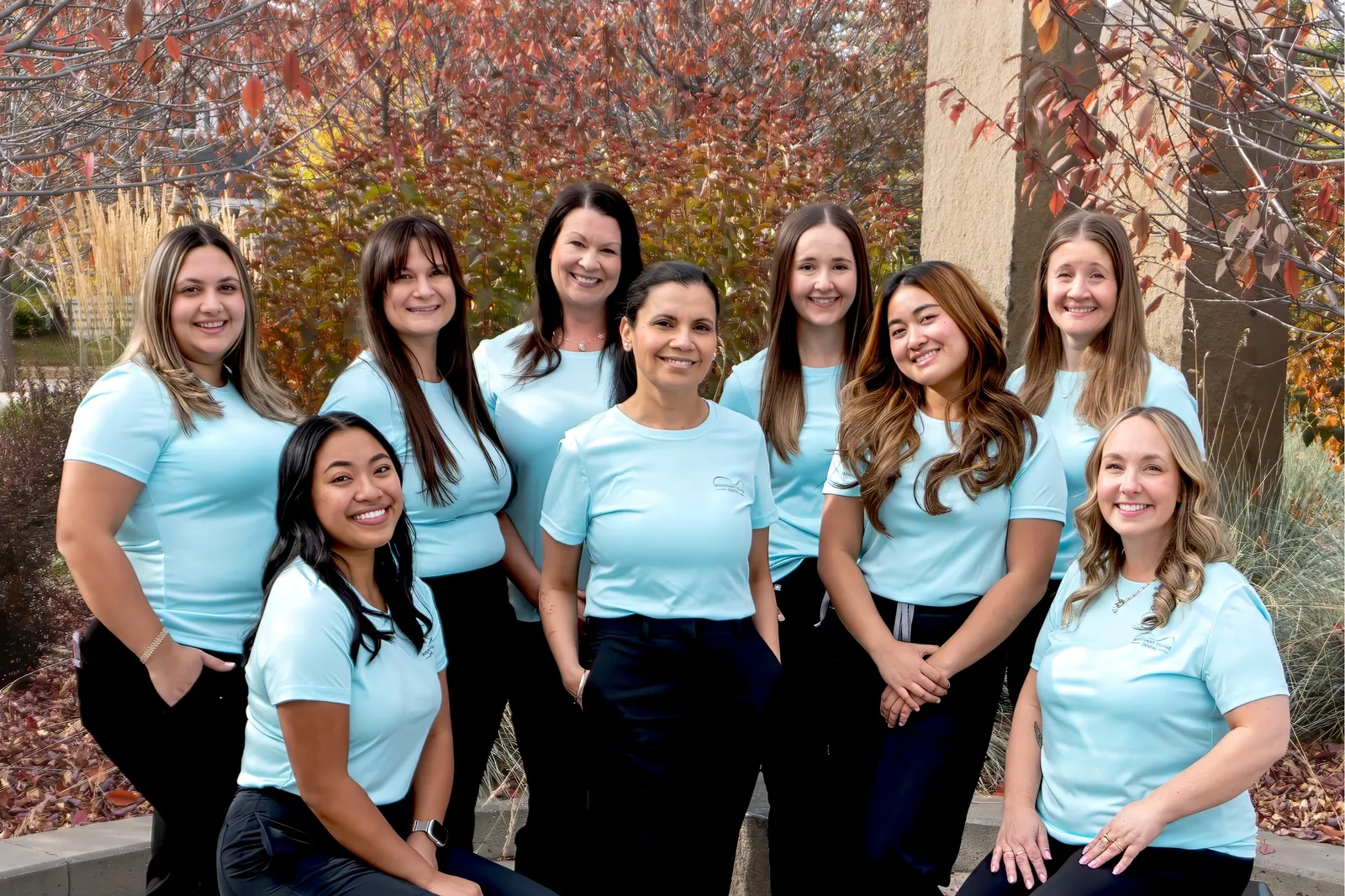 The Mahogany Village Dental team smiling together outdoors among autumn trees